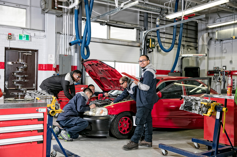 centennial college students smiling in a garage while working on a car