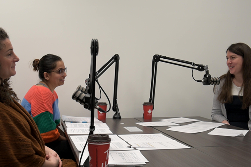 Three female speakers sitting behind a desk with microphones