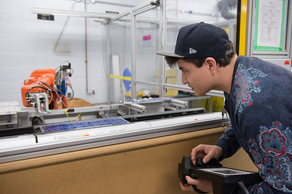Male Information and Communication Engineering Technology student holds the door of a wiring system and points to its content inside