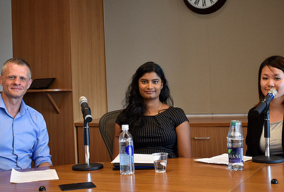Three podcast speakers sitting behind a desk with microphones