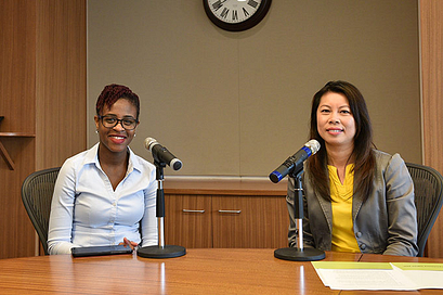 Two female speakers sitting behind a desk with microphones