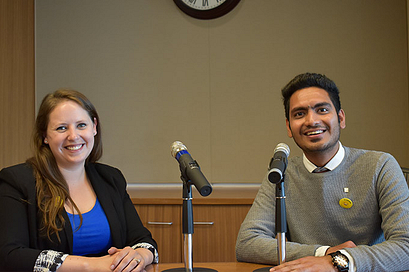Two speakers sitting behind a desk with microphones