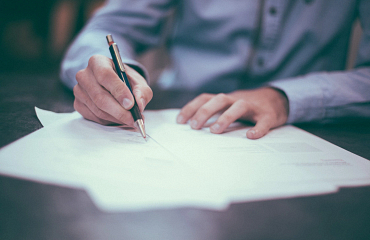 a person writing on paper in front of a computer