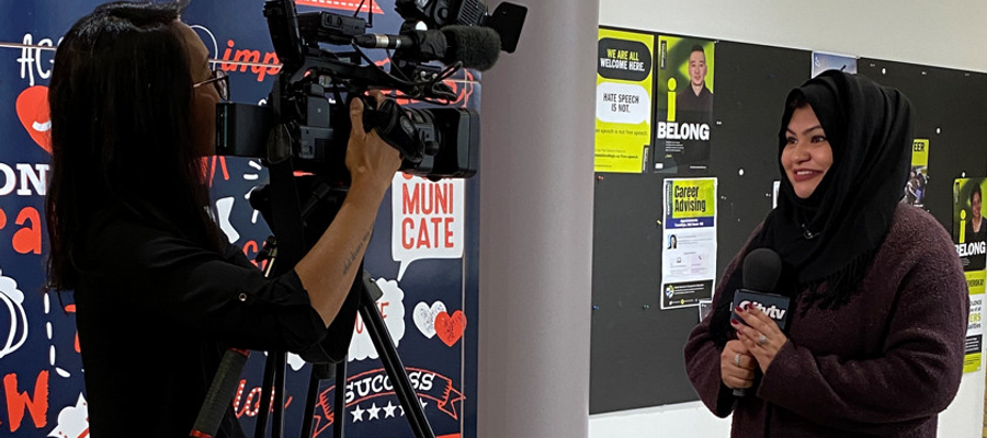 A student films another student holding a microphone while speaking to the camera