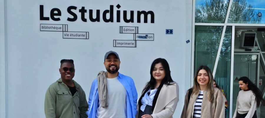 four people pose outside in front of a building named Le Studium