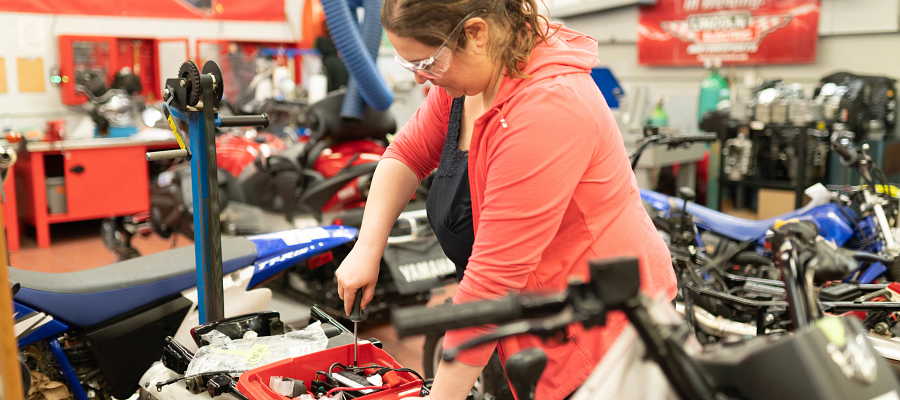 Female Centennial College student working on a broken motorcycle