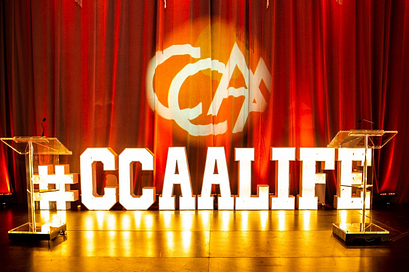 舞台上有写着“CCAA生活”的大字，CCAA的标志投影在后墙上的幕布上