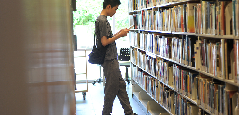An image of a person standing in a bookshelf aisle at Morningside campus Library.