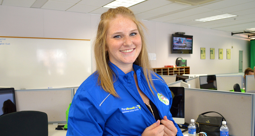 centennial college sports journalism student smiling while wearing a paralympics jacket in the story arts centre journalism lab