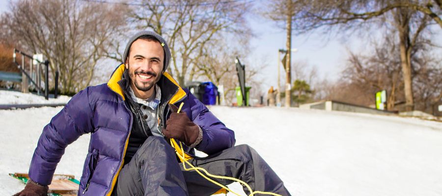 An international student smiling while posing on a snow sled
