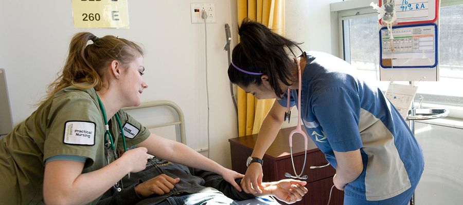 Practical nursing student helps another nursing student to check a patient's vital signs during lab practice at Morningside campus