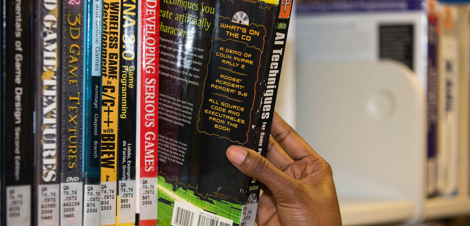a hand pulling a book from the shelf in the library for the grab & go service