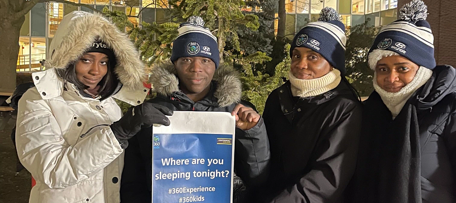 a group of stuensts posing outside in toques and coast with a sign