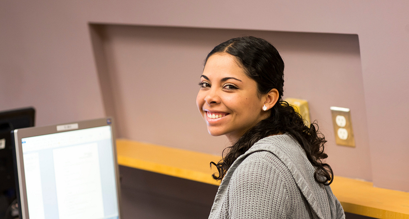Centennial College student smiling while applying to a bursary on a computer