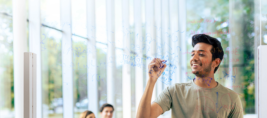 student smiling as they're writing on a glass whiteboard in the story arts centre library