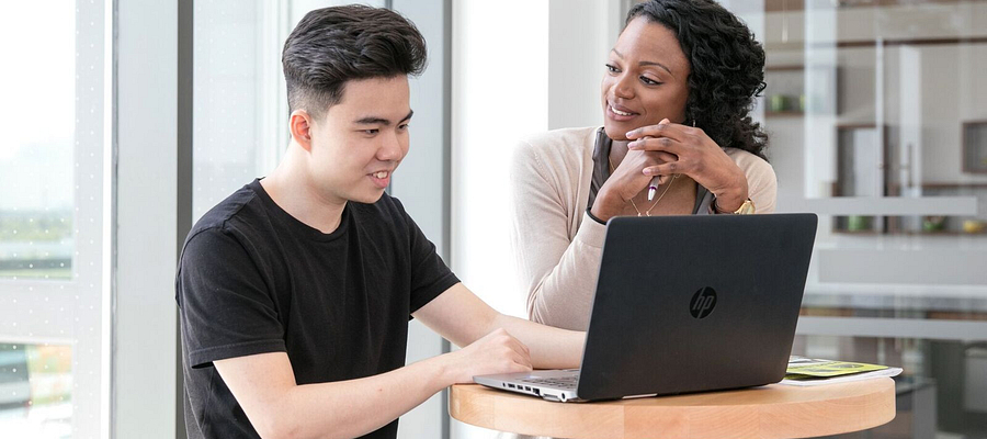 Centennial College student smiling and meeting with an advisor while working on a laptop