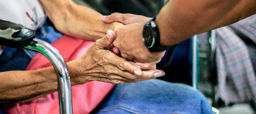 elderly lady sitting down holding hands with another person