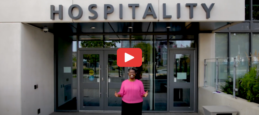 An image of a YouTube video where an African woman is standing outside a Hospitality building