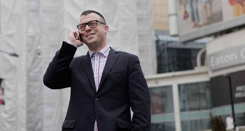 a Centennial College Public Relations Corporate Communications program graduate wearing business professional and talking on a cellphone outside in a city setting