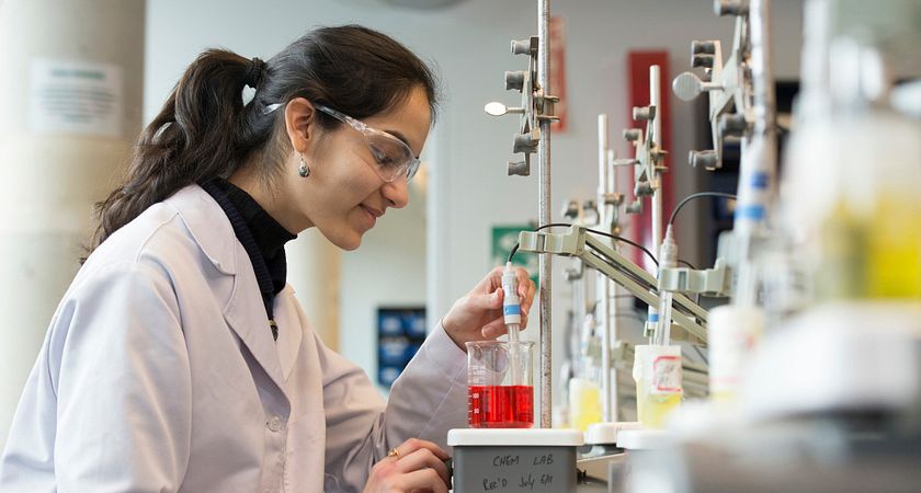 Female Food Science student adjusts the pH level of a red solution in the chemistry lab.